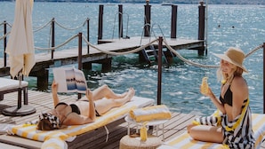 Een houten steiger met ligbedden en parasols, met uitzicht op een wateroppervlak.