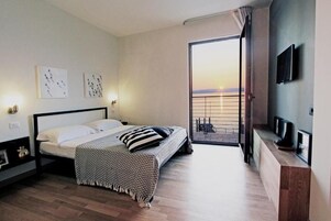 Ein modernes Schlafzimmer mit Bett, Kunstwerk an der Wand, Fernseher und Balkon mit Aussicht.