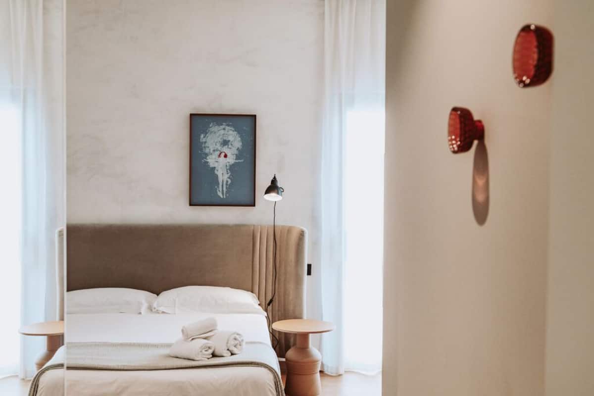 Een keurig opgemaakt slaapkamer met een bed, nachtkastjes, een lamp en een wanddecoratie.
