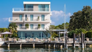 Een modern, meerhoog hotel met balkons, een zwembadgedeelte met ligbedden en een steiger die in het water uitstekt.