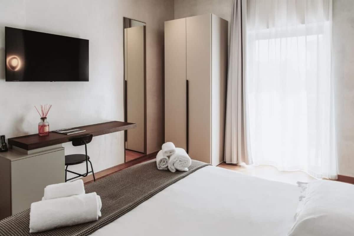 Een hotelkamer met een bed, een bureau, een stoel, een televisie, een kledingkast en een raam met gordijnen.