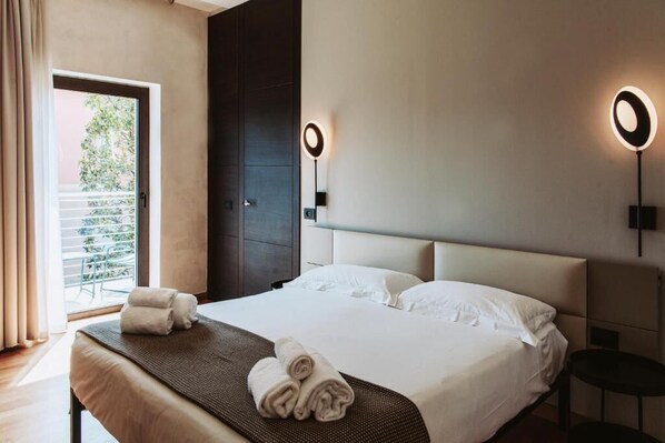 A hotel room with a large bed, two bedside tables, a window with curtains, and two wall-mounted lights. - AQVA Boutique Hotel (Adults Only) - Sirmione (Sirmione)