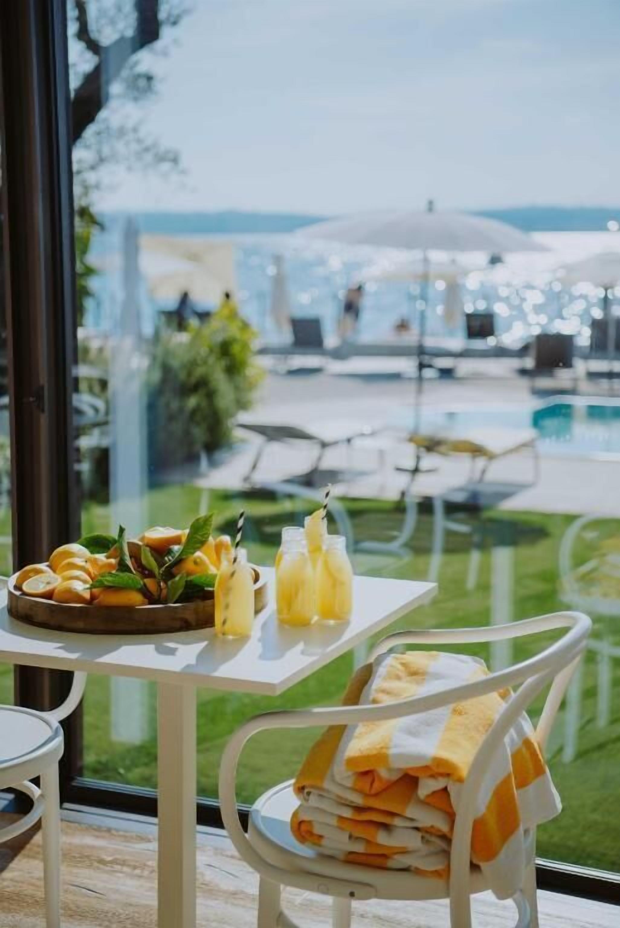A table with a fruit bowl, drinks, and towels, overlooking a pool area.