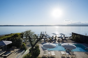 A poolside area with lounge chairs and umbrellas, overlooking a calm body of water.