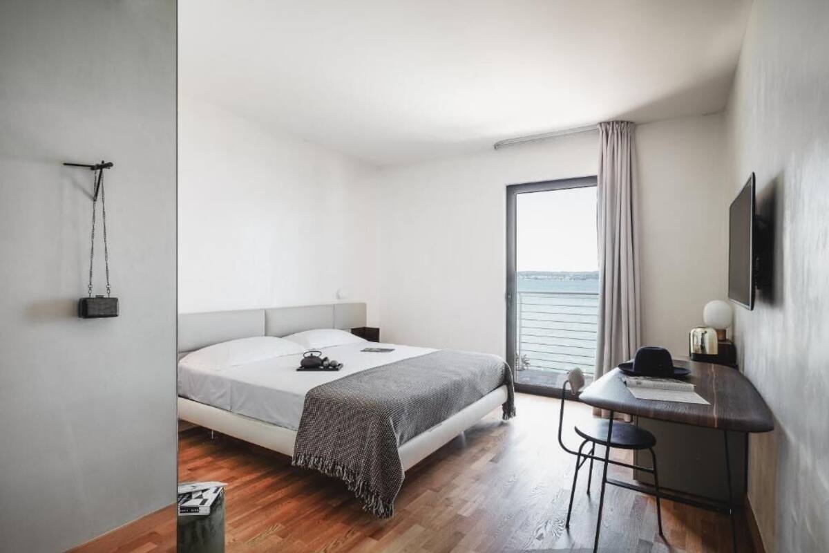Een minimalistisch ingerichte slaapkamer met een bed, bureau en uitzicht op zee.