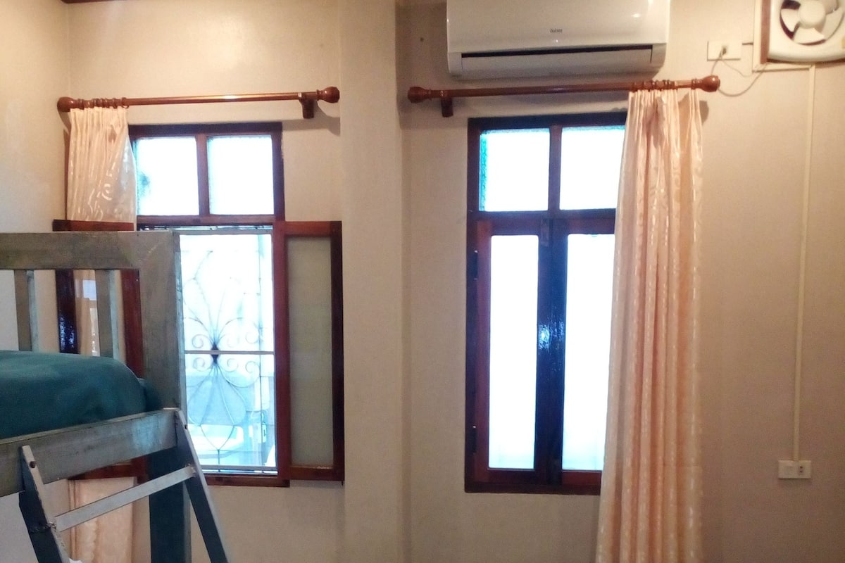 A room with bunk beds, a ladder, and two windows with curtains.