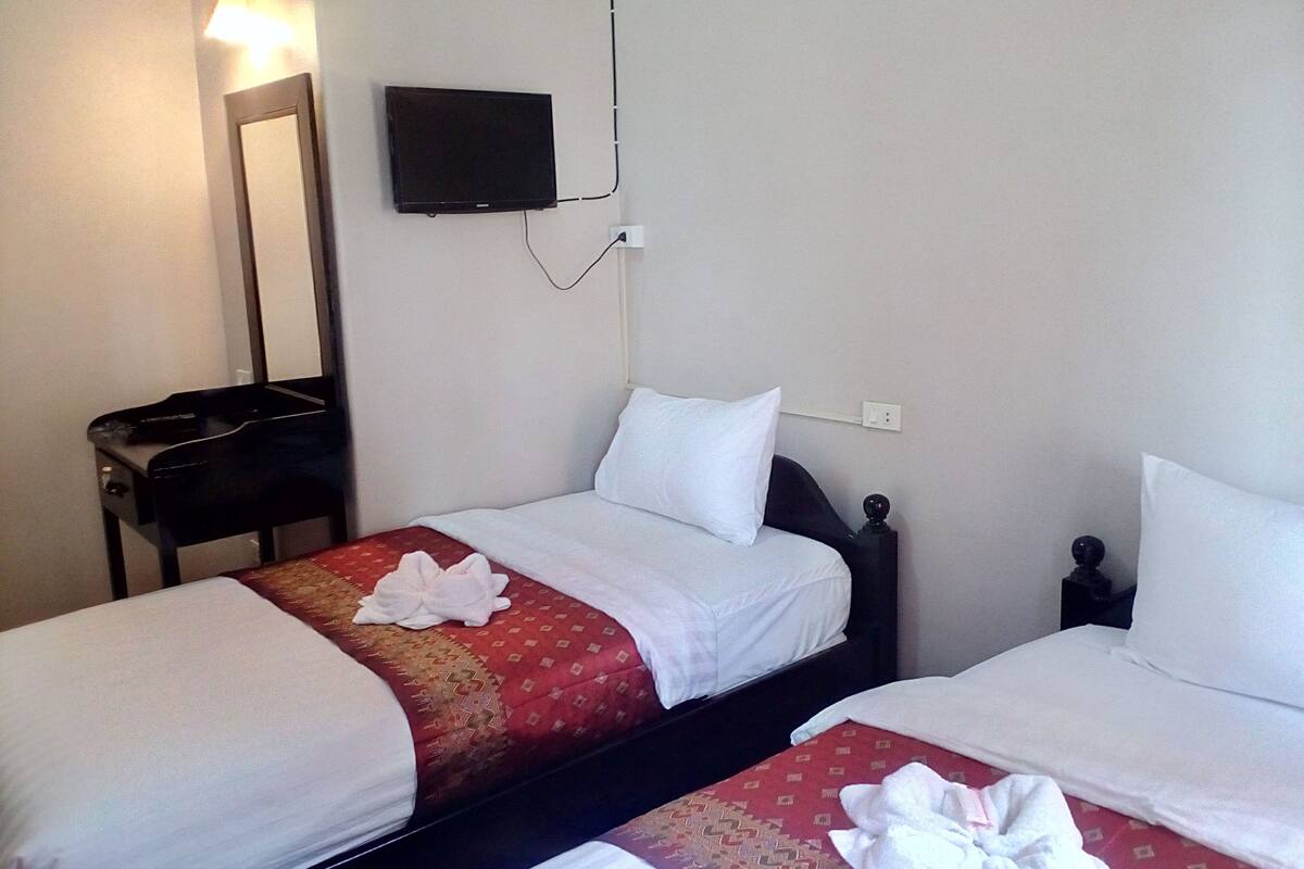 A hotel room with two beds, a TV mounted on the wall, and a small table with a remote control.