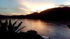 A sunset over a calm lake with a silhouette of a mountain range in the background. - Sokmisay Hotel・GuestHouse (Luang Prabang)