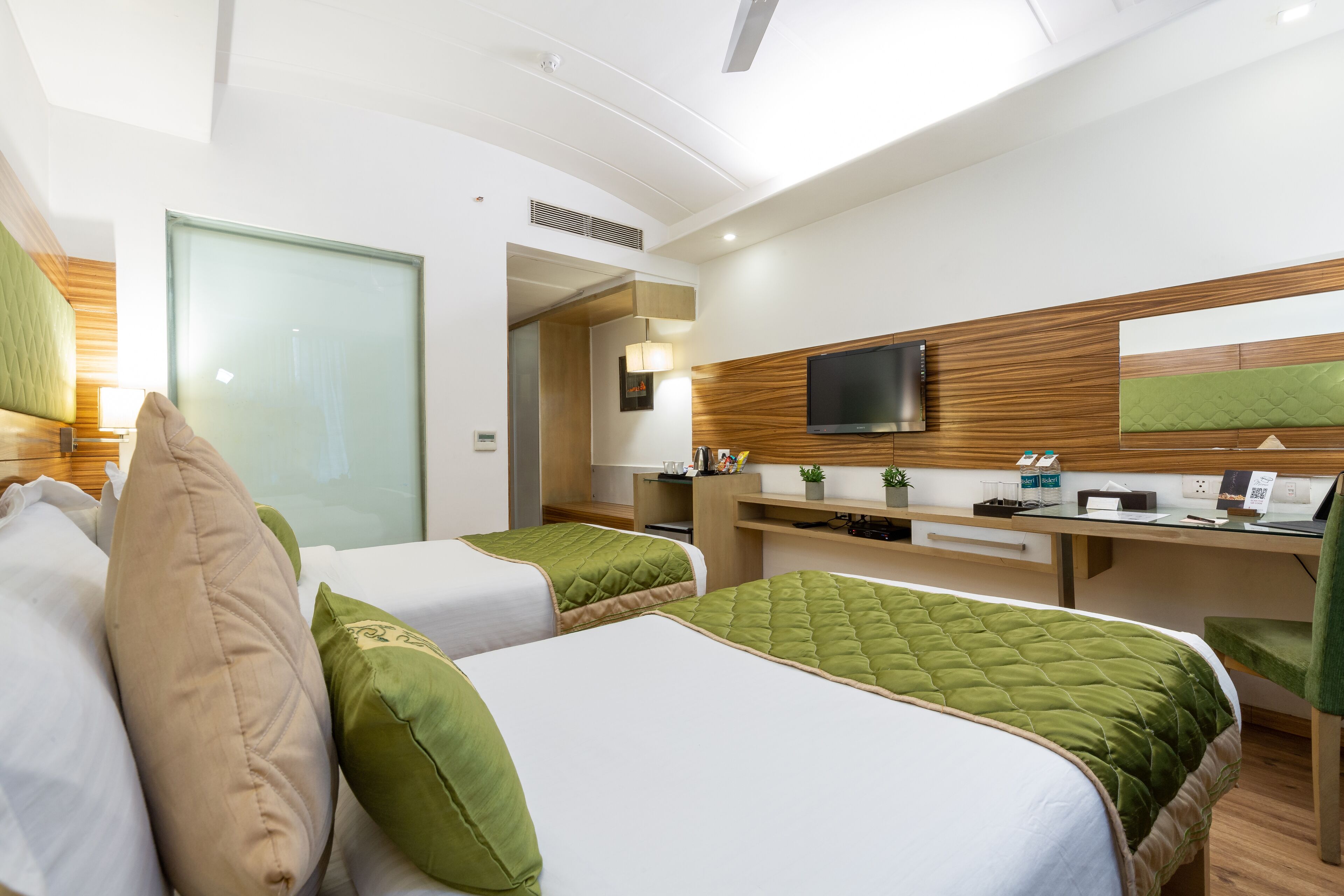 Une chambre d’hôtel avec deux lits, un bureau avec un ordinateur, une télévision et une petite plante.