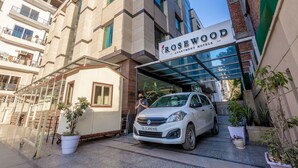 A Rosewood apartment building with a white car parked in front. - Rosewood Apartment Hotel - Gurgaon (Gurugram)