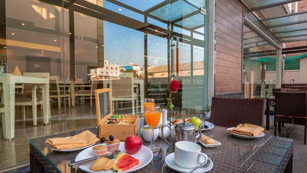 A breakfast table with plates, glasses, and a fruit bowl. - Rosewood Apartment Hotel - Gurgaon (Gurugram)