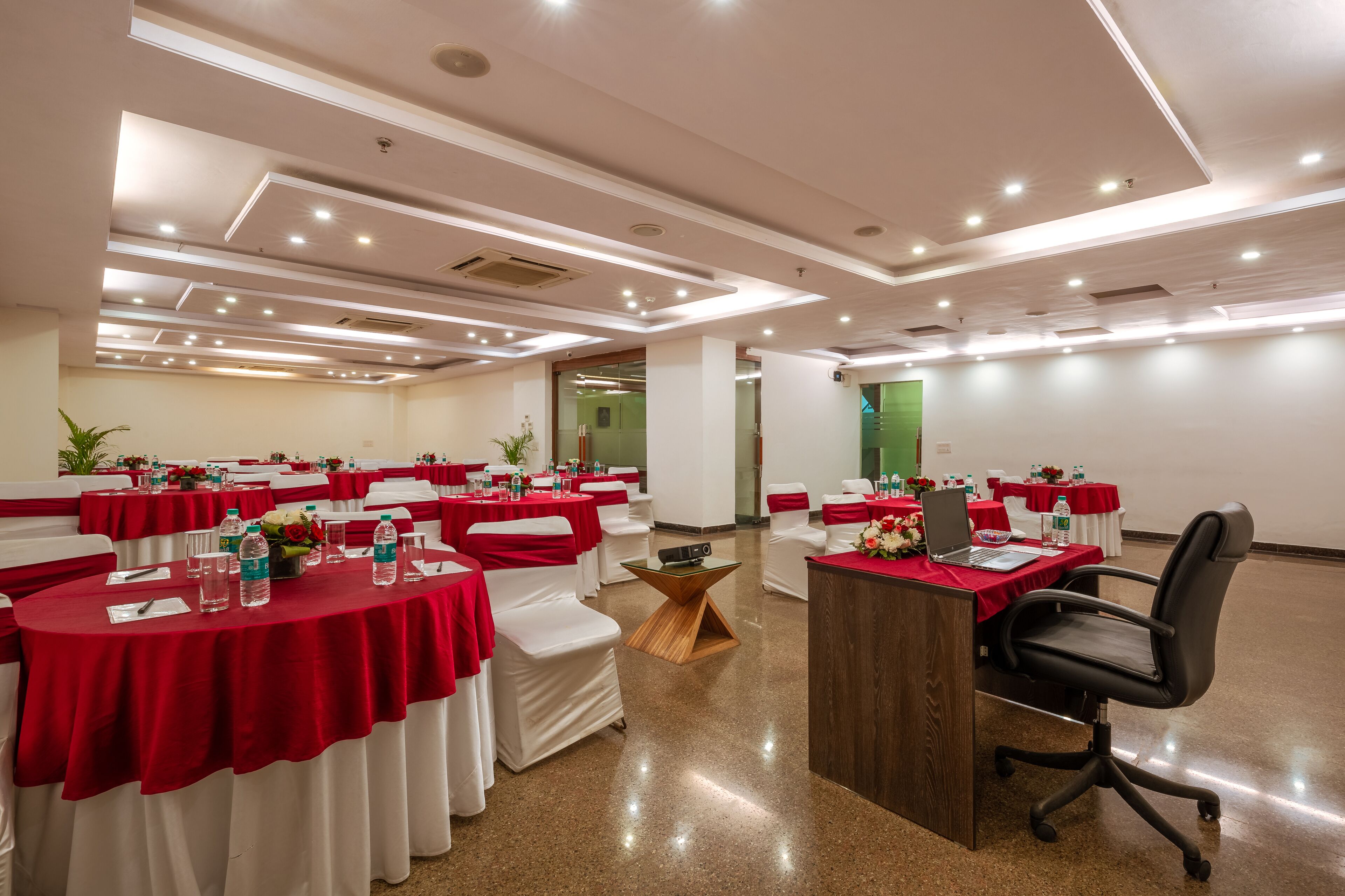 A conference room with round tables, white chairs, and red tablecloths. There is a wooden podium and a laptop on one table.
