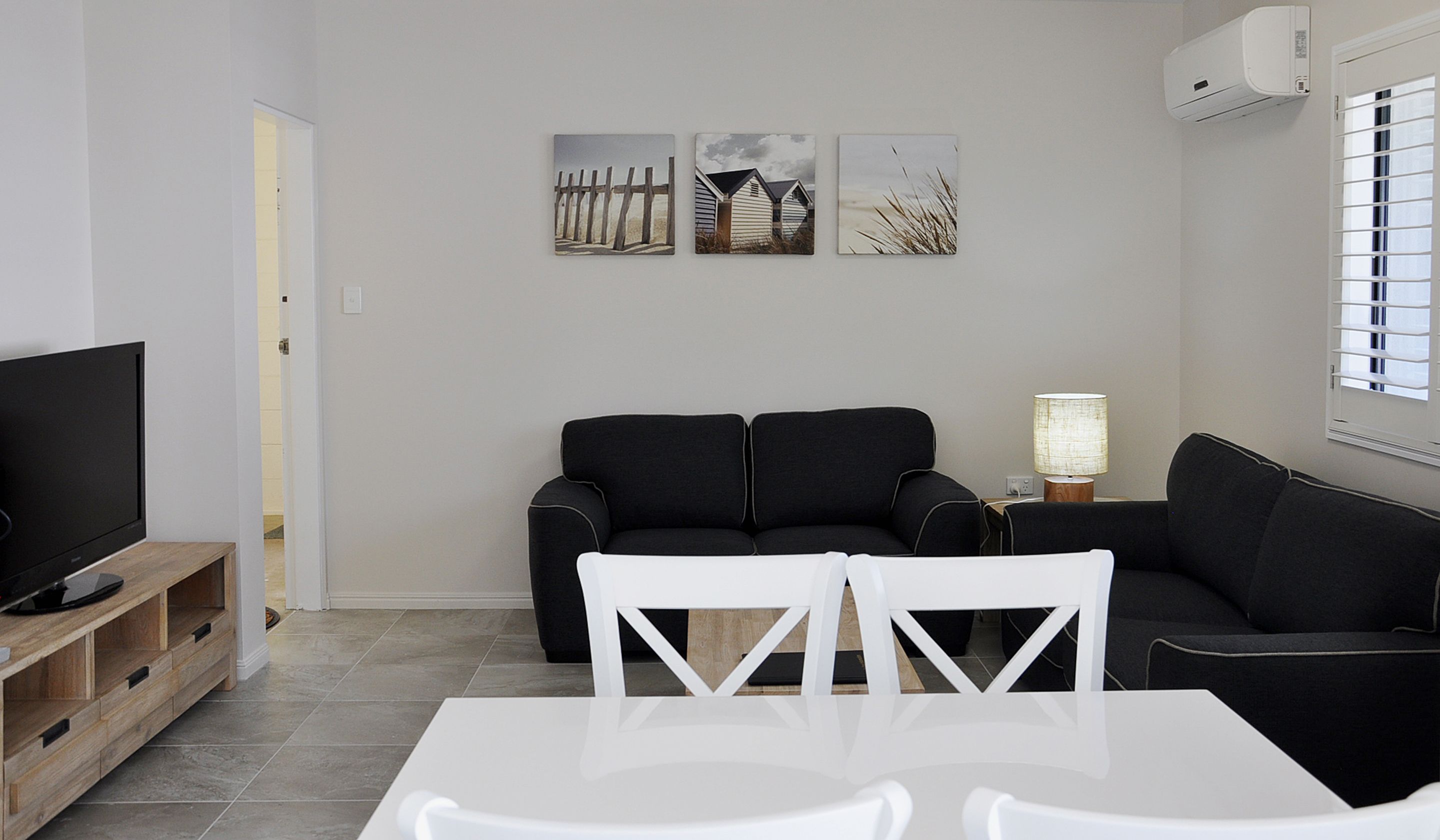 A modern living room with a black sofa, a white dining table, and a TV on a wooden stand.