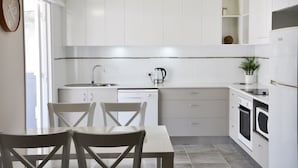 A modern kitchen with white cabinets, a dishwasher, a coffee maker, and a dining area with a table and chairs. - Angelwaters (North Ward)