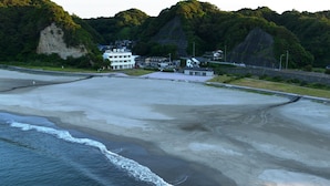 A coastal area with a sandy beach, a road, and buildings in the background. - Ryokan Urashima (Iwaki)