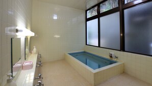 A bathroom with a bathtub, a sink with a mirror, and a window with frosted glass. - Ryokan Urashima (Iwaki)