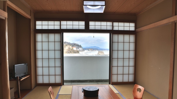 A traditional Japanese room with tatami flooring, a low table, and a television on a shelf. - Ryokan Urashima (Iwaki)