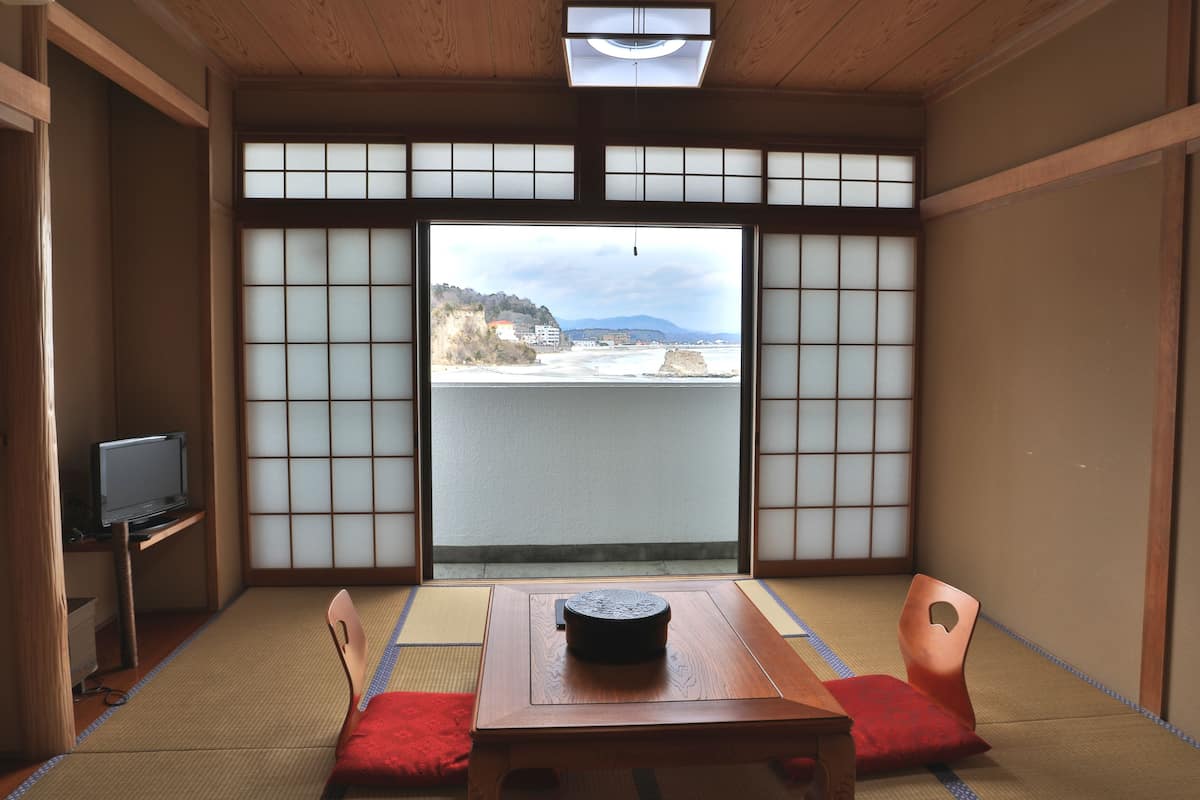 A traditional Japanese room with tatami flooring, a low table, and a television on a shelf.