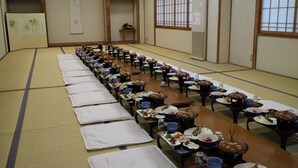 A traditional Japanese room with tatami mats, low tables, and a long table set for a meal. - Ryokan Urashima (Iwaki)