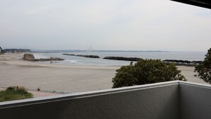 A beach view from a balcony with a clear sky, distant buildings, and a rocky outcrop. - Ryokan Urashima (Iwaki)