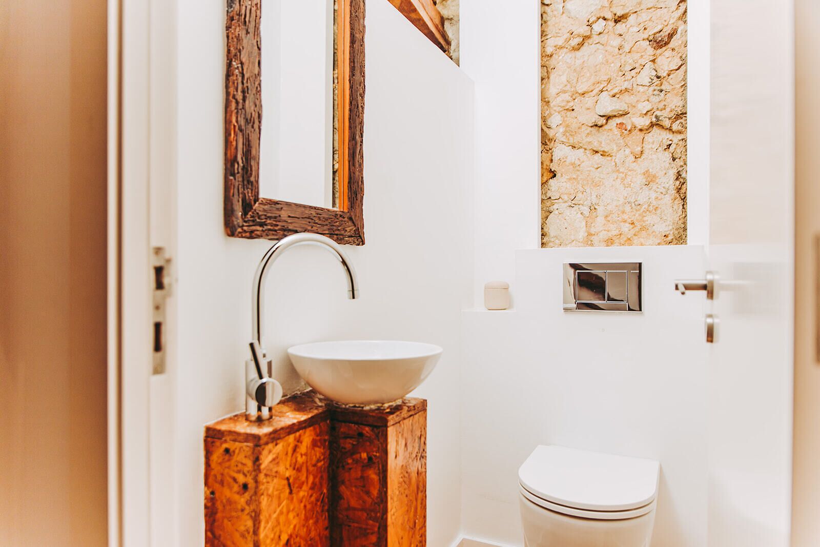 A bathroom with a wooden vanity, a white sink, a mirror, and a toilet.