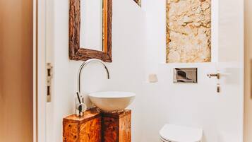 A bathroom with a wooden vanity, a white sink, a mirror, and a toilet.