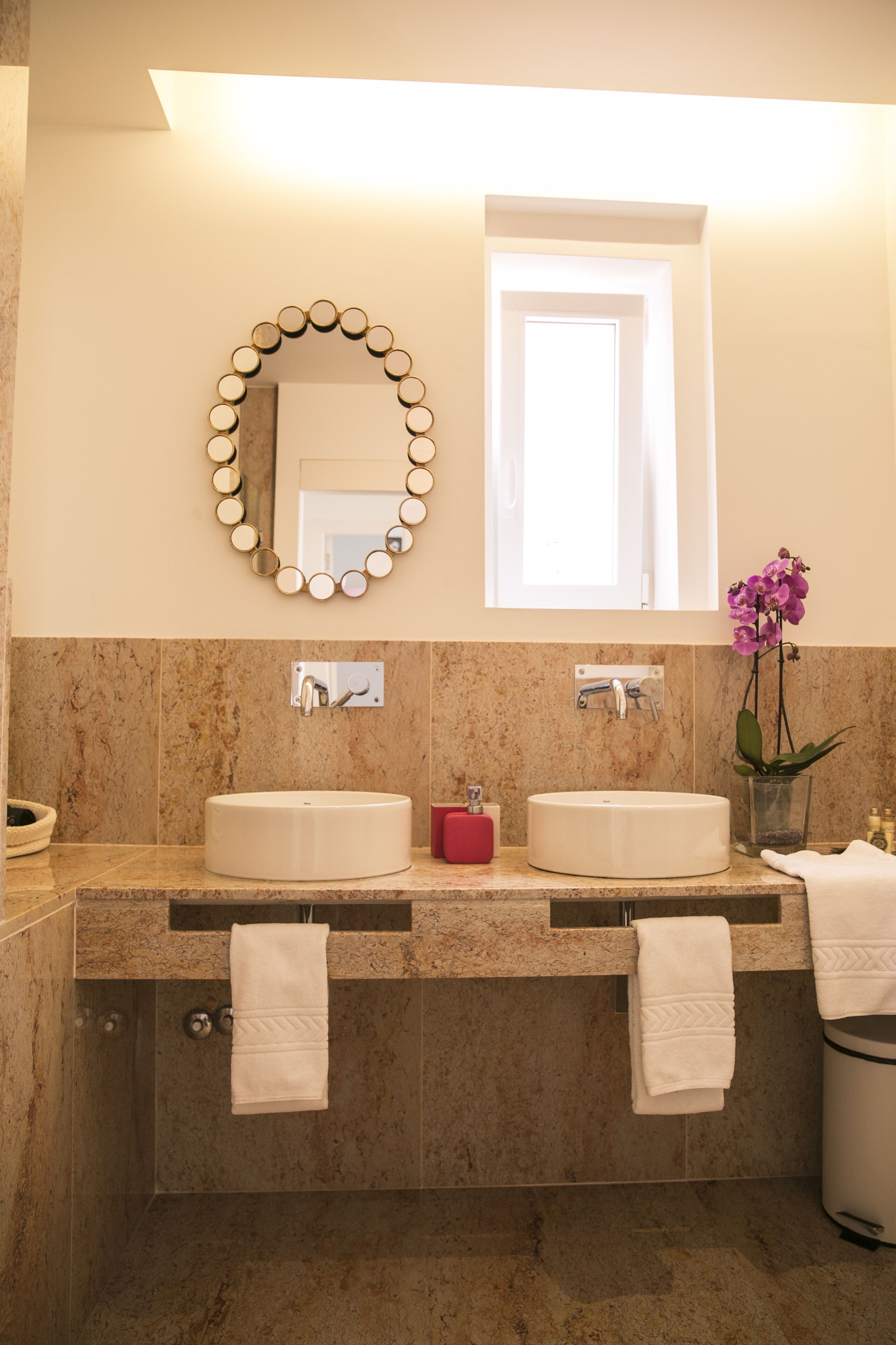 Un bagno con due lavandini, uno specchio, una finestra e un'orchidea in vaso.