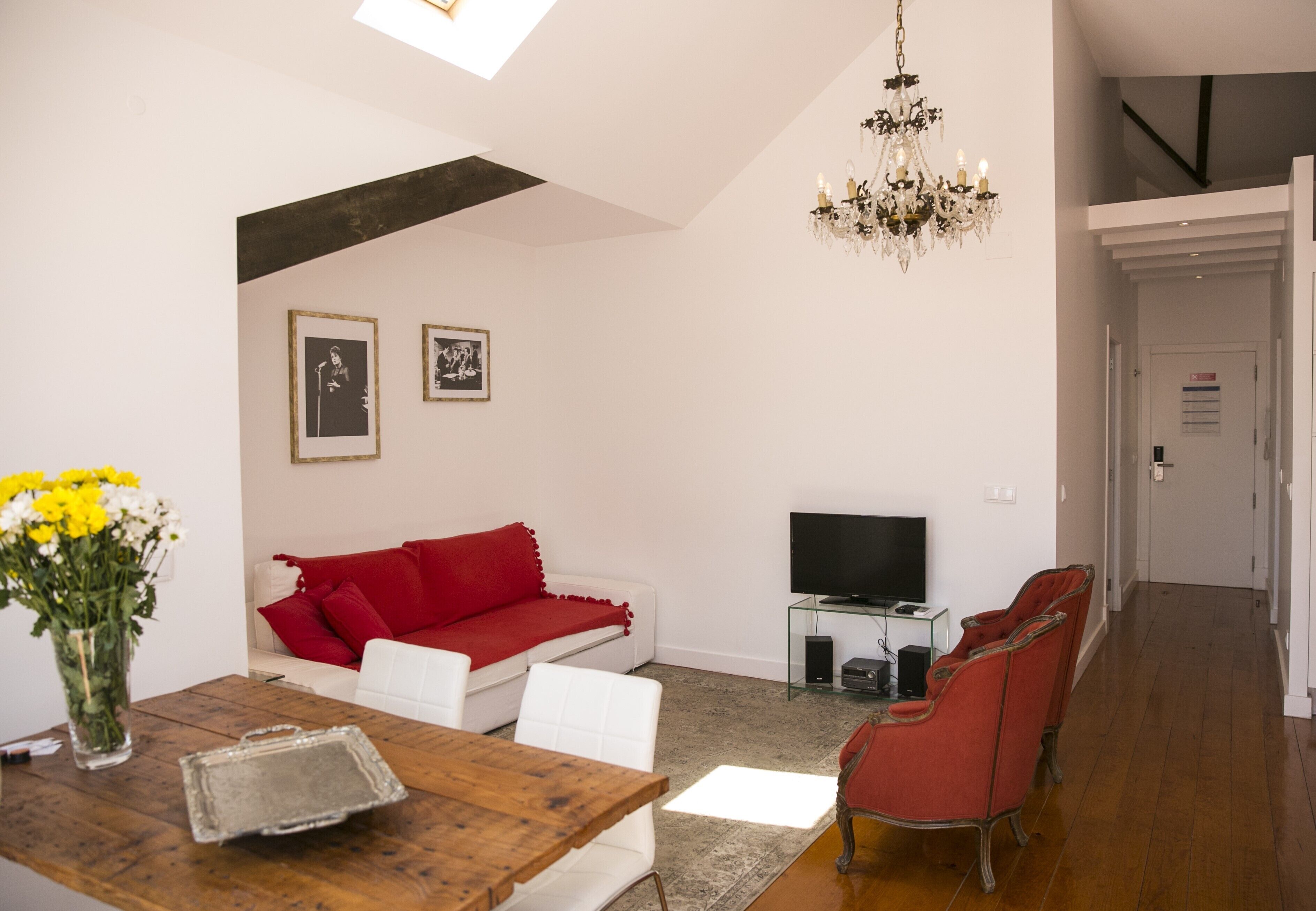 Un salon moderne avec une table à manger en bois, un canapé blanc, des chaises rouges, un lustre et un téléviseur à écran plat.
