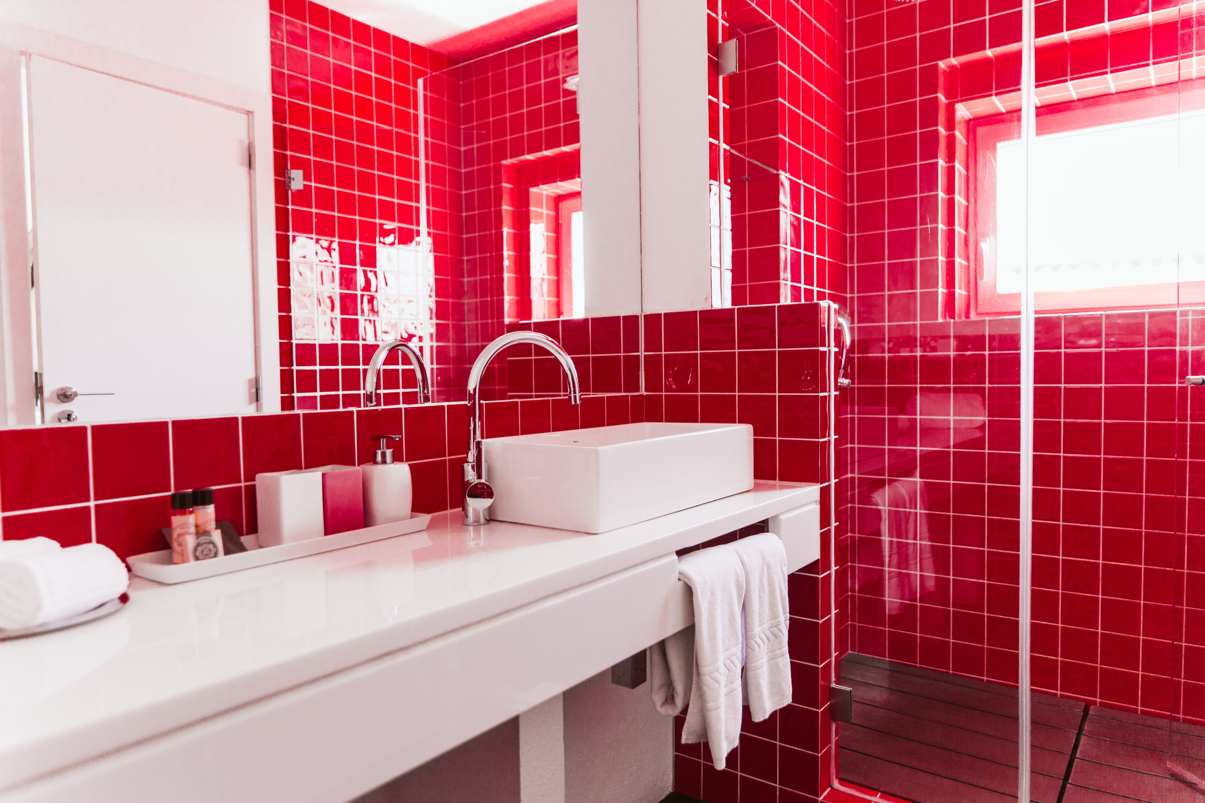 A modern bathroom with red tiles, a white sink, and a glass shower enclosure.