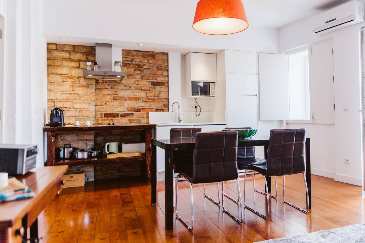 A compact kitchen with a brick wall, modern appliances, and a dining area with chairs and a table.