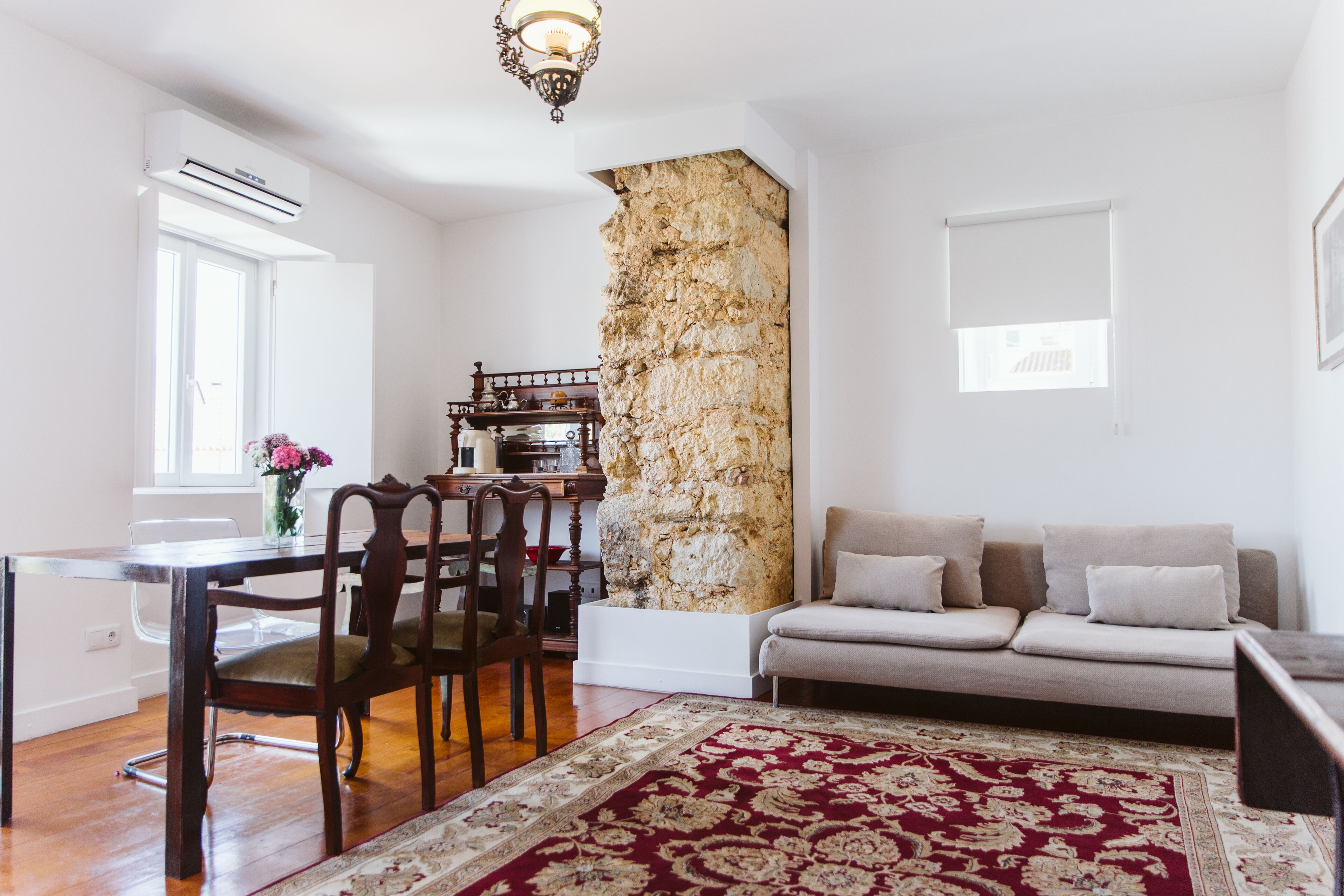 Una sala de estar con una pared de acento de piedra, un sofá, una mesa de comedor con sillas y un tapete estampado.