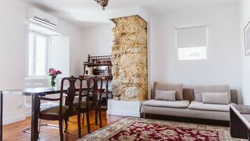 Una sala de estar con una pared de acento de piedra, un sofá, una mesa de comedor con sillas y un tapete estampado.