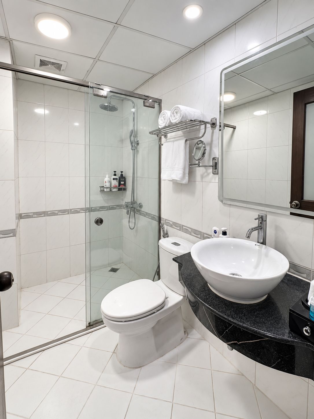 Un baño moderno con ducha envuelta en vidrio, inodoro blanco, lavabo grande y espejo.