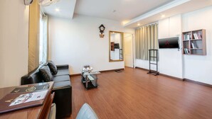 Quarto de hotel moderno com piso de madeira, sofá de couro preto, mesa de centro de vidro, TV de tela plana na parede e estante de livros.