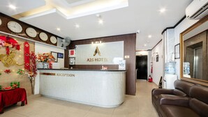 Uma área de recepção de hotel, com balcão de atendimento, sofá e um relógio de parede mostrando a hora em várias cidades.