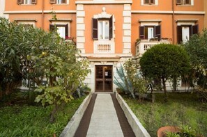Um edifício com entrada central, ladeado por vegetação e um caminho que leva à porta.