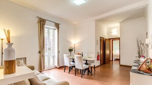 Un vaste espace de vie comprenant une table à manger, des chaises blanches et un canapé. Une grande fenêtre, agrémentée de rideaux, laisse entrer la lumière naturelle.