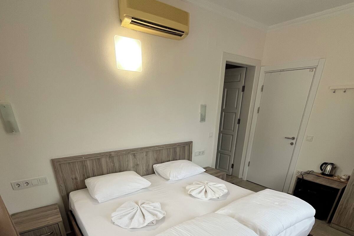 A hotel room with a bed, bedside tables, an air conditioning unit, and a door.