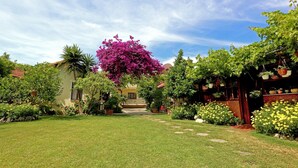 Un jardin bien entretenu, avec une variété de plantes et de fleurs, un chemin dégagé et, au fond, un bâtiment doté d’un toit en tuiles.