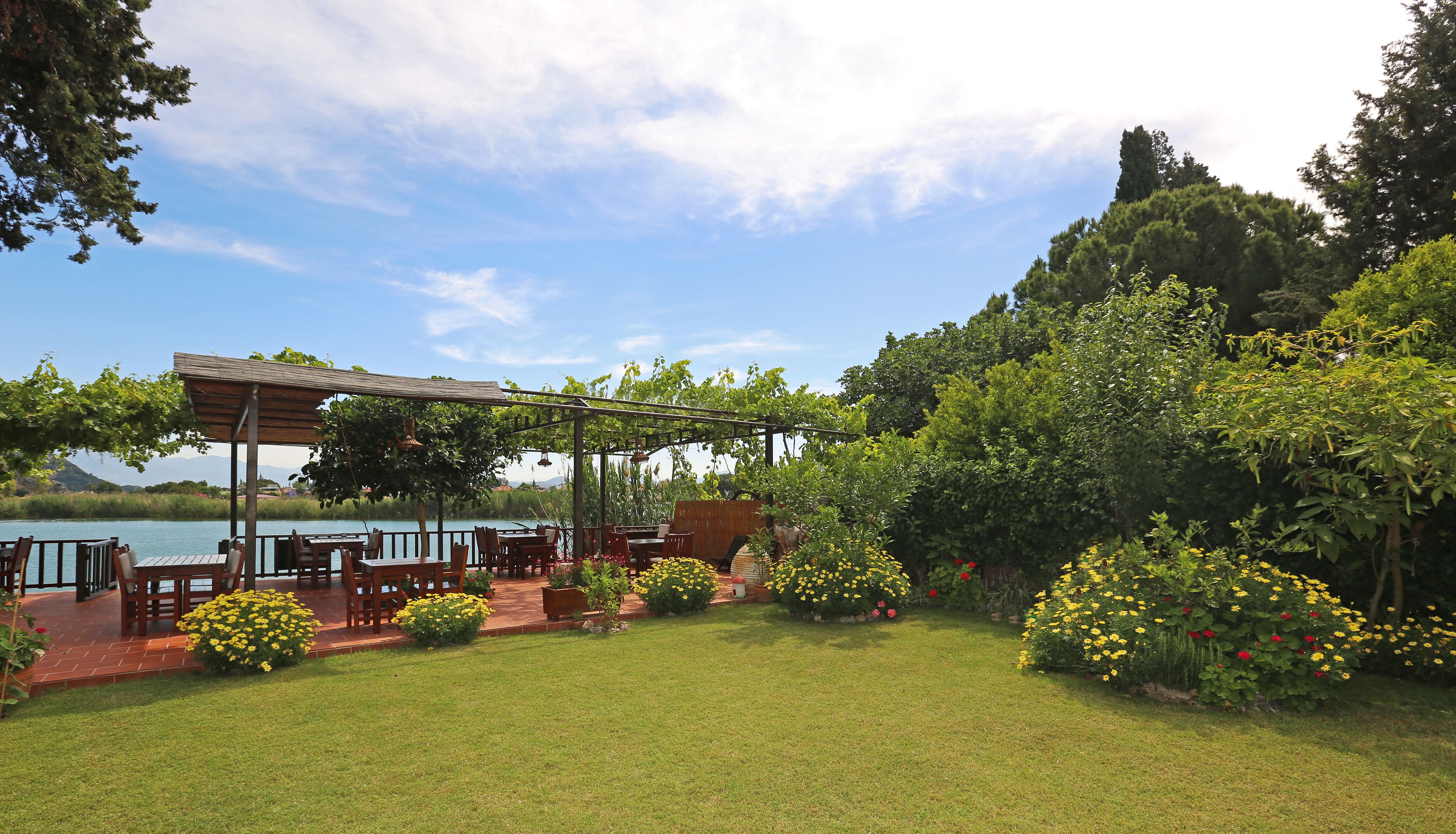 Ein Garten mit einer Pergola, Sitzgelegenheiten im Freien und Blick auf ein See.