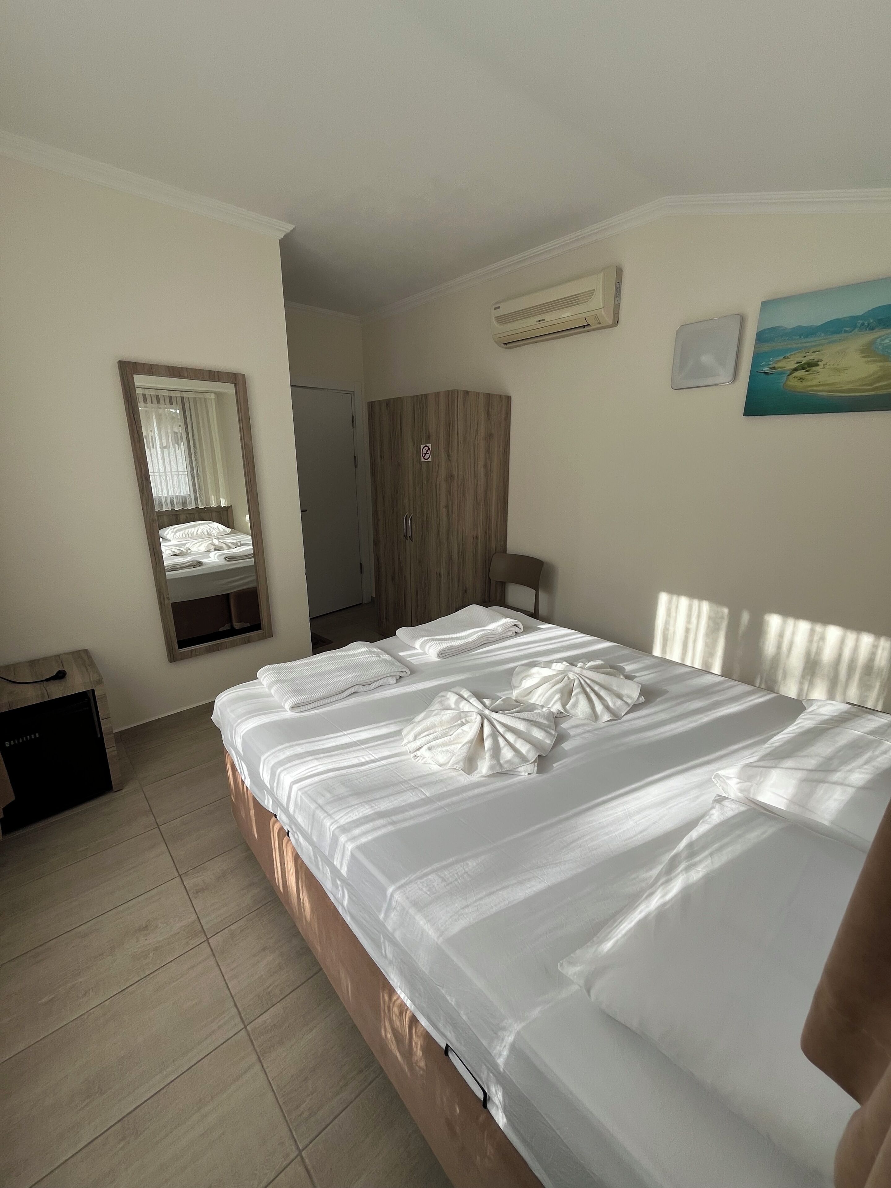 Una habitación de hotel con una cama, un armario, un espejo, un cuadro y un calefactor.