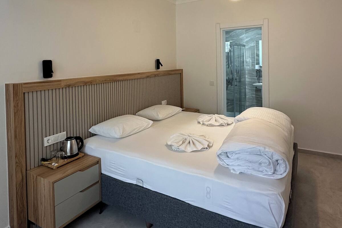 A hotel room with a bed, bedside table, and a view of the bathroom through a glass door.