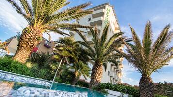 Un hôtel doté d’une piscine entourée de palmiers, avec un ciel bleu et dégagé.