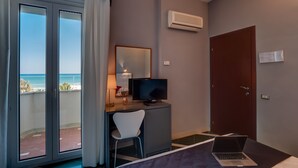 A hotel room with a bed, a desk with a chair, a television, and a laptop. There is a sliding door leading to a balcony with a view of the ocean. - Hotel Metropol (Senigallia)