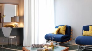 A modern living room with a blue sofa, a white chair, and a coffee table with decorative items. - Hotel Metropol (Senigallia)