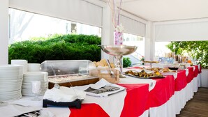 A buffet setup with various food items, a large metal bowl, and a glass display case, all covered with a red and white tablecloth. - Hotel Metropol (Senigallia)