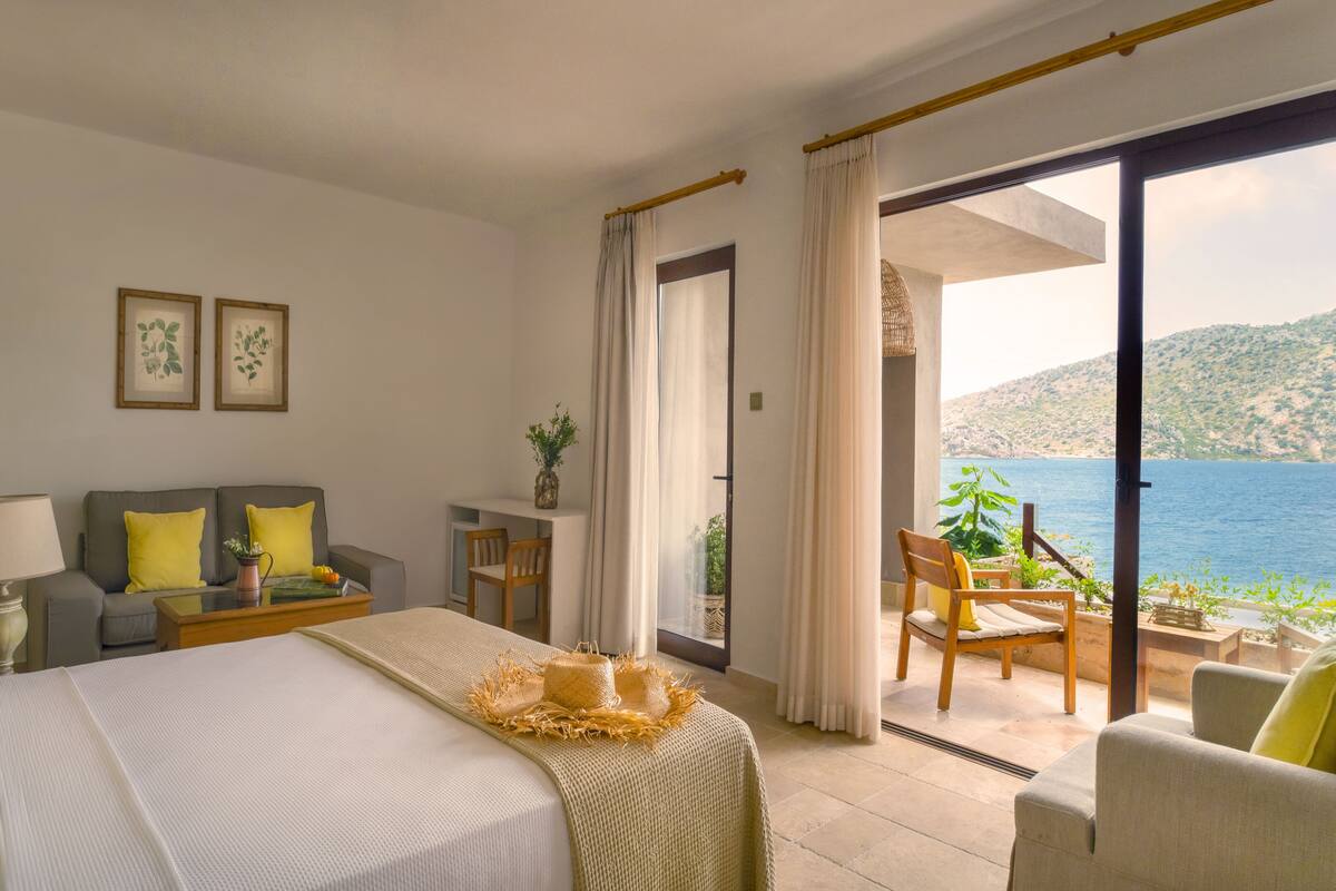 Ein Hotelzimmer mit Bett, Sofa, Tisch und Stuhl. Ein Balkon bietet Blick aufs Meer.