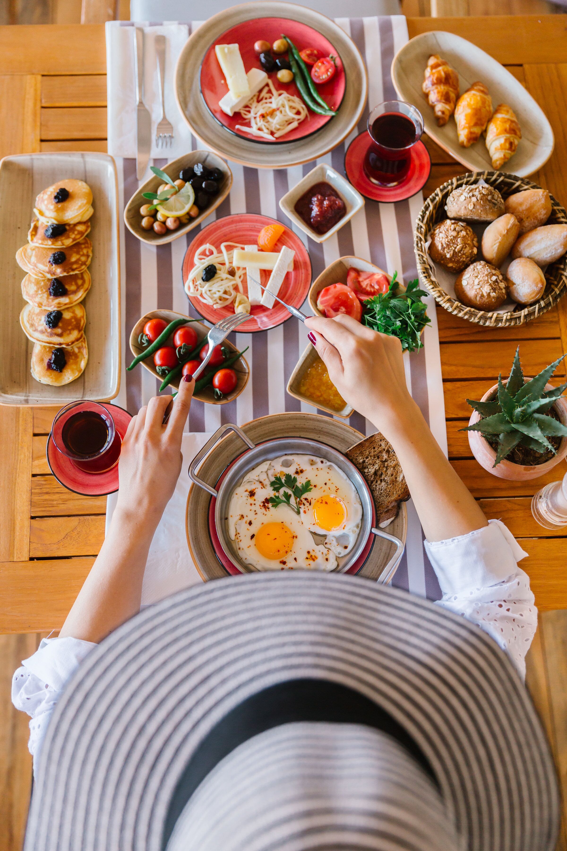 Een ontbijttafel met pannenkoeken, eieren, brood en diverse toevoegingen.