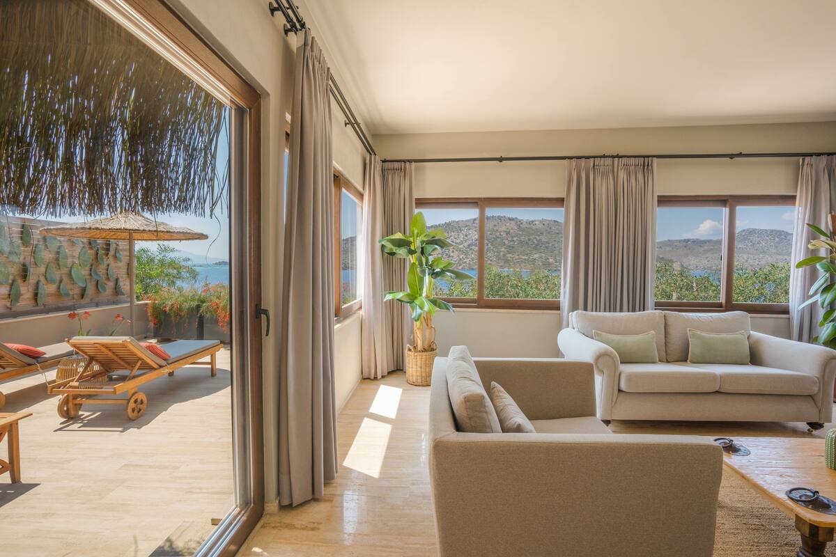 Ein großzügiger Wohnbereich mit großem Fenster, einer Couch, einem Couchtisch und einer Liege.