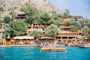Un hotel frente al mar con varios balcones, mobiliario exterior y una zona de piscina.